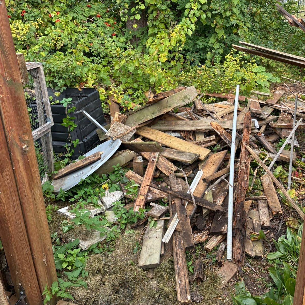 Demolished deck and fence debris piled in an Ottawa backyard: split pressure-treated boards, rotten joists and deck planks stacked beside a compost bin, ready for removal.