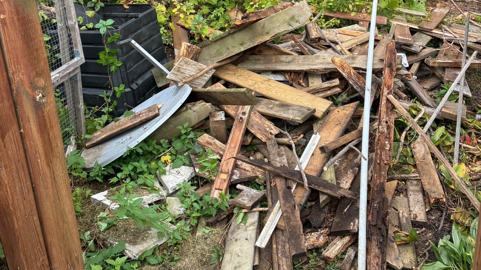 Demolished deck and fence debris piled in an Ottawa backyard: split pressure-treated boards, rotten joists, deck planks and metal posts stacked beside a compost bin, ready for removal.