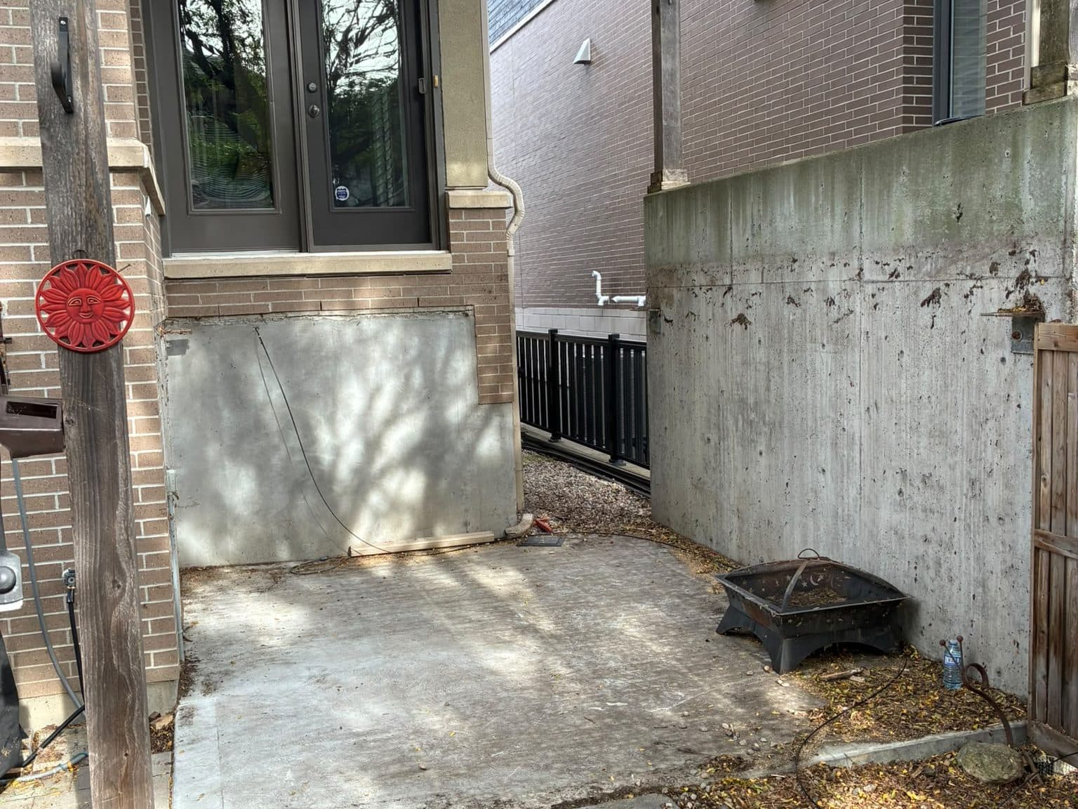 The same patio after the deck and steps came out, concrete pad swept clear to the door, pergola posts still standing against the brick.